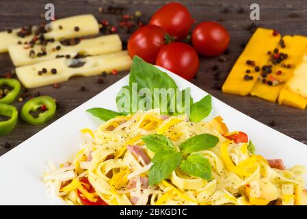 Tagliatelle pasta with pesto sauce, bacon, Gauda, Cheddar, Emmental cheese and basil leaves in white plate on grey wooden background. Close up image - Stock Photo
