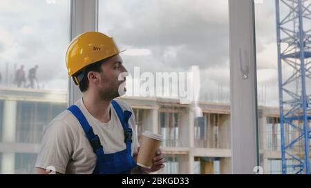 Worker wearing hardhat taking a break drinking coffee. Stock Photo