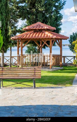 Summer garden with furniture set and wooden summerhouse. Green trees, mown grass. Blurred water background near monastery of St. Nicholas, Lake Vistonida, Porto Lagos, Xanthi region in Northern Greece Stock Photo