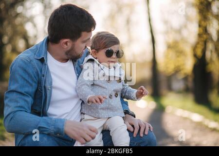 Cute daughter sitting on father's lap. Portrait of dad and daughter in the park Stock Photo