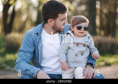 Cute daughter sitting on father's lap. Portrait of dad and daughter in the park Stock Photo