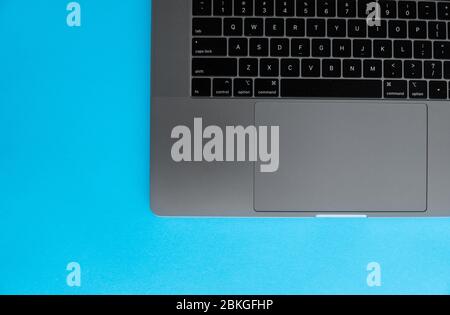 Keyboard of a silver laptop that lying on a blue background. Stock Photo