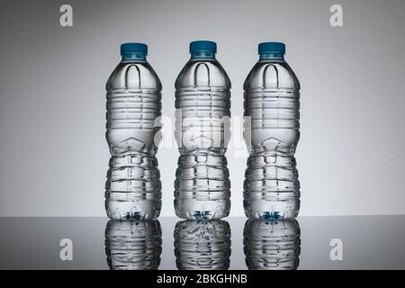 Clear plastic water bottles with no labels in a row against a plain neutral background. Single bottle version available Image ID: 2BKGH Stock Photo