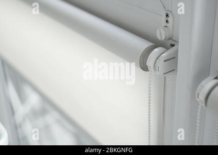 Details of white fabric roller blinds on the plastic window with wood texture in the living room. Stock Photo