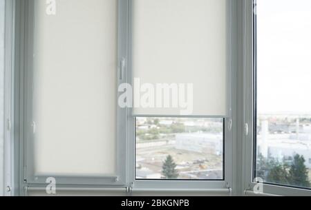 Details of white fabric roller blinds on the plastic window with wood texture in the living room. Stock Photo
