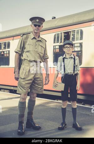 Severn Valley Railway 1940s wartime WW2 summer event UK. Retro vintage front view 1940s man in uniform & young boy standing by train, station platform. Stock Photo