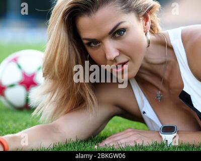 Girl in fitness clothes lies on grass stadium Stock Photo
