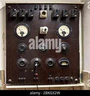 A vintage switchboard featuring a voltmeter and ammeter, as well as several circuit breakers and sockets, mounted in a weathered wooden frame. Stock Photo