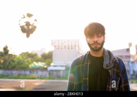 Young handsome bearded Indian hipster man in urban streets Stock Photo
