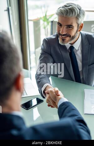 Businessmen shaking hands in office Stock Photo