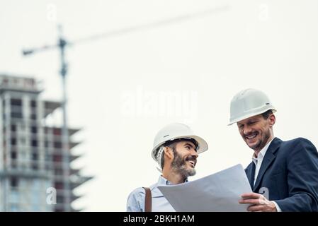 Male architects discussing blueprint at construction site Stock Photo