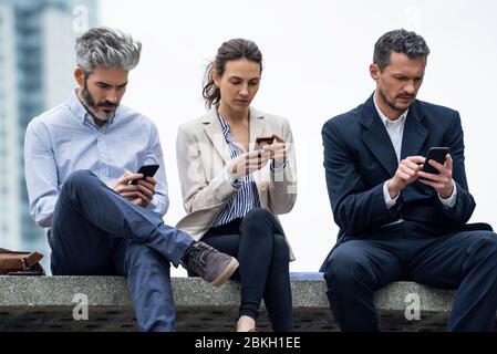 Business people using smartphones in public park Stock Photo