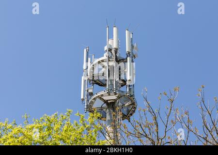 View on the top part of a mobile phone / telecommunications mast. Used for transmitting signals and data. E. g. for 5G networks. Blue sky background. Stock Photo