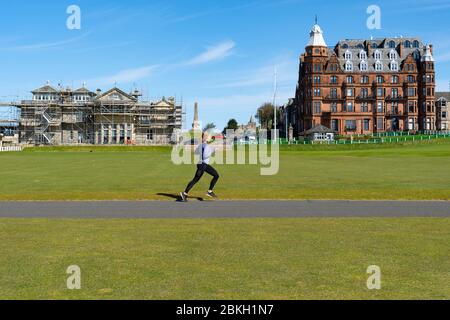 St Andrews, Scotland, UK. 4 May 2020.  The famous Old Course at St Andrews is closed due to the coronavirus lockdown. Locals are making the most of the closed golf course by using it as a park for they daily exercise. Woman runs across first and eighteenth fairways.  Iain Masterton/Alamy Live News Stock Photo