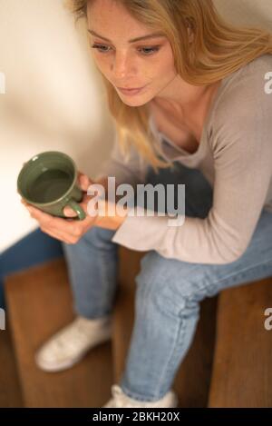 Young woman holding cup while sitting on steps Stock Photo