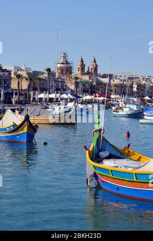 Colourful Maltese fishing boats in the sheltered harbour at Marsaxlokk, Malta. Inhabited for centuries, the village is a popular tourist destination. Stock Photo