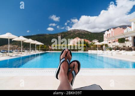 Odyssey Hotel, Agia Efimia, Cephalonia island, Greece - July, 14 2019: Close up view of young woman feet in Tommy Hilfiger blue flip-flops lying on a Stock Photo