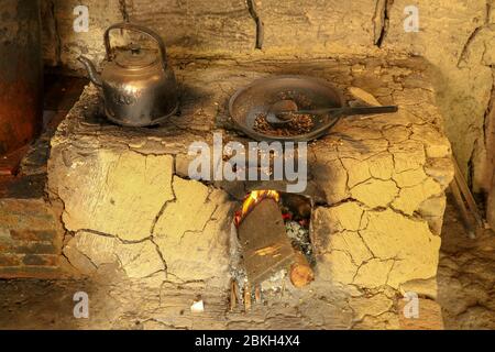 Traditional clay furnace with open fireplace. Primitive way of roasting coffee beans in steel pan at coffee farm in Bali, Indonesia. Simple production Stock Photo