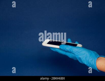 men's hand in medical gloves hold phone on blue background. Stock Photo