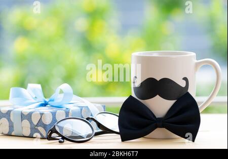 Happy fathers day concept. beautiful gift box, glasses and coffee cup with black mustache on wooden table over green bokeh background. Stock Photo