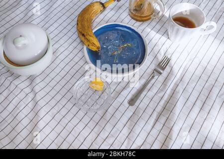 Crumbs and food object on table with blue ceramic plate and yellow banana on table with white clerical tablecloth. Stock photo. Stock Photo
