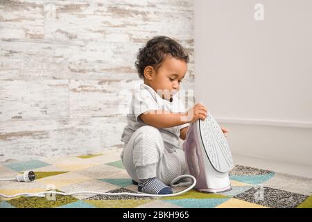 Little African-American baby playing with iron at home. Child in danger Stock Photo