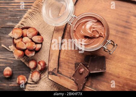 Jar with tasty chocolate paste and hazelnuts on table Stock Photo