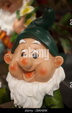 Cute dwarf living in a garden. Smiling garden gnome decoration against a blurry background. Funny elf in the garden. Happy dwarf figurine. Stock Photo