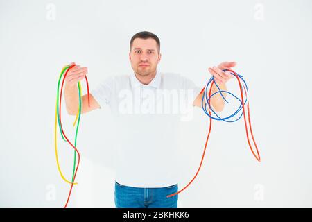 Young man isolated over white background. Confused guy hold colorful electrical cords. Good for reusing and recycling. No waste lifestyle for better Stock Photo