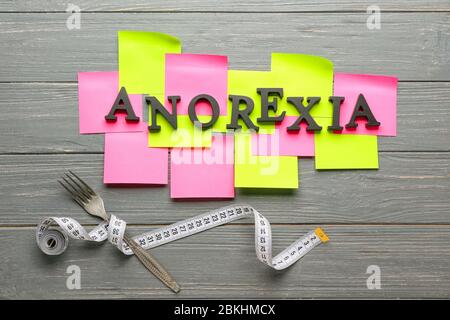 Word ANOREXIA, papers, fork and measuring tape on wooden background Stock Photo
