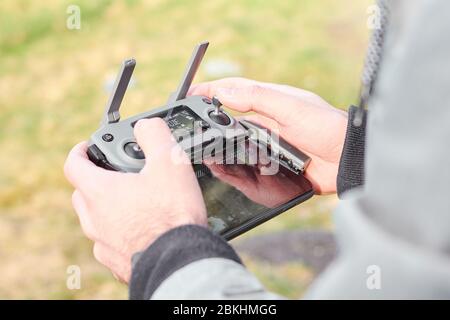 Close up mans hands holding drone remote controller with smartphone in the field. Concept of aerial shooting and flying, San Francisco, May 2020. Stock Photo