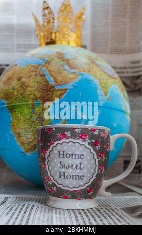 Mug with globe, golden crown, representing Covid-19, and newspapers on bokeh background. Stock Photo