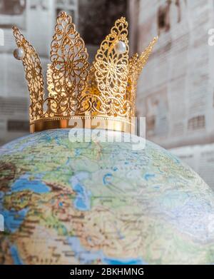 Golden crown with pearls representing Covid-19 on a globe with bokeh newspaper background. Stock Photo