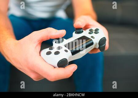 Young man sit in room during quarantine. Cut view and close up of hands holding joystick or gamepad in hands. Pushing buttons and playing on it Stock Photo