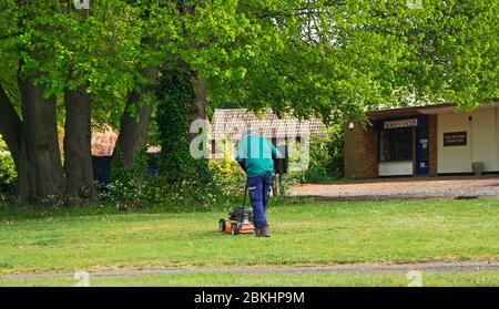 A man engaged in grass cutting on a small green in a residential area in Hellesdon, Norfolk, England, United Kingdom. Stock Photo
