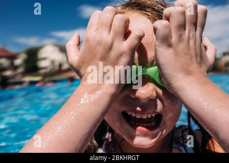 close up of young child pushing goggles on to face at pool