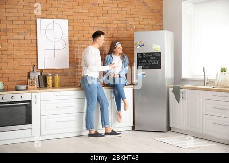 Happy couple near chalkboard with written menu on refrigerator in kitchen Stock Photo