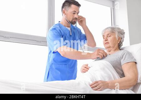 Male doctor working with elderly patient in hospital room Stock Photo