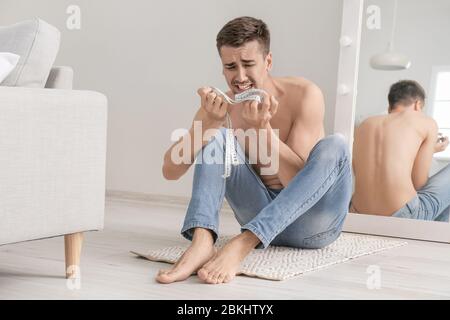 Young man suffering from anorexia with measuring tape at home Stock Photo