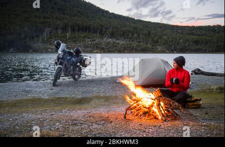 Woman enjoying campfire at camp next to still lake in Tierra del Fuego Stock Photo