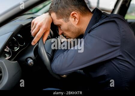 The man is very tired of driving a car and sleeping on the steering wheel Stock Photo