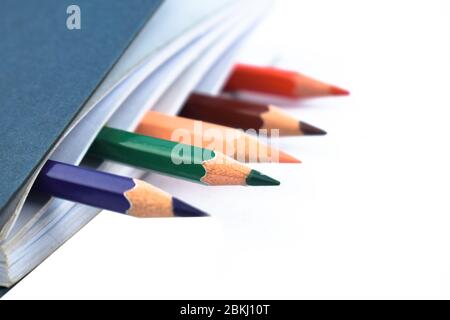 Five different colored wood pencil crayons placed in a simple white paper notebook Stock Photo