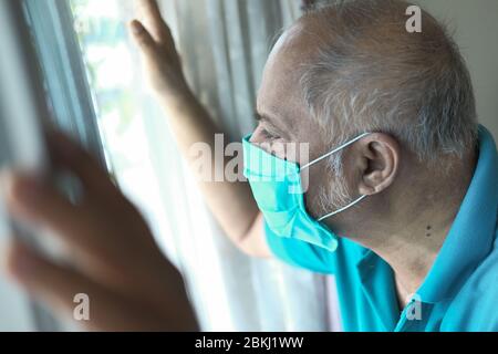 senior man with face mask looking through window  Stock Photo