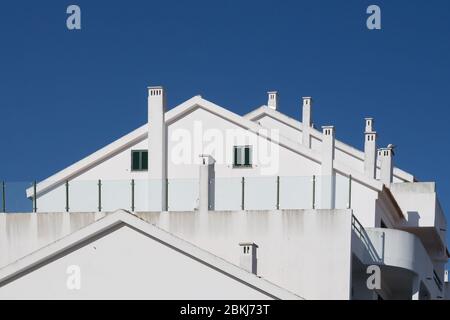 Lines of the white painted houses with many chimneys. Modern construction. Bright blue clear sky. Alvor, Algarve, Portugal. Stock Photo