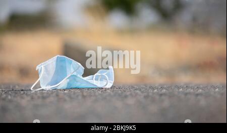 Discarded medical face mask stuck into road - concept of unhygienic dispose of masks helps to spread covid-19 or coronavirus. Stock Photo
