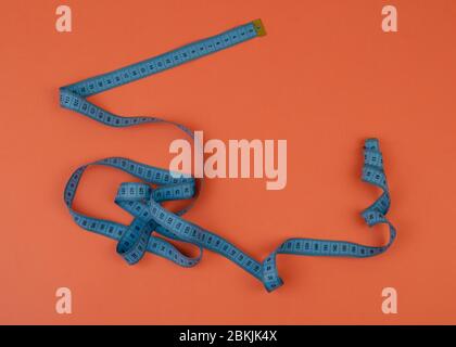 Blue tailor measuring tape on orange background with copy space. Frame with empty space for your design. Stock Photo