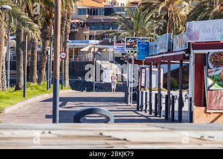 A solitary woman walks on the promenade during the covid 19 lockdown in the tourist resort area of Costa Adeje, Tenerife, Canary Islands, Spain Stock Photo