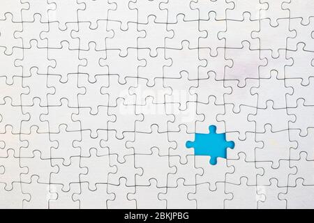 Blue background showing through missing piece in white jigsaw puzzle. Stock Photo