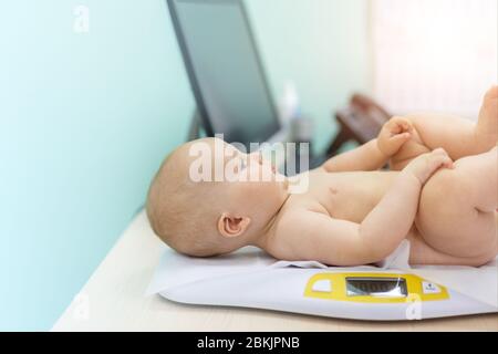 Pediatrician specialist taking measurement infant child weight during screening examination. Cute caucasian baby lying on electronic scales doctors