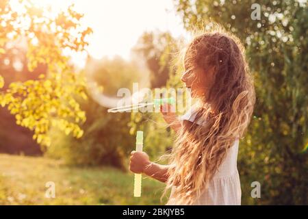 Little cute girl blowing bubbles in spring park. Kid having fun playing games outdoors. Children activities Stock Photo